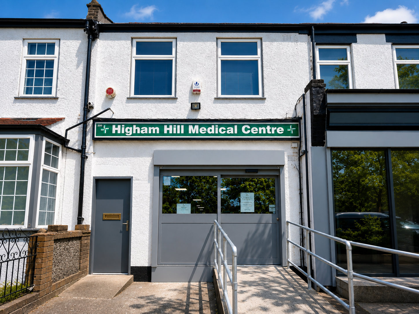 The front of Higham Hill Medical Centre, showing the green practice sign and the step-free ramped entrance