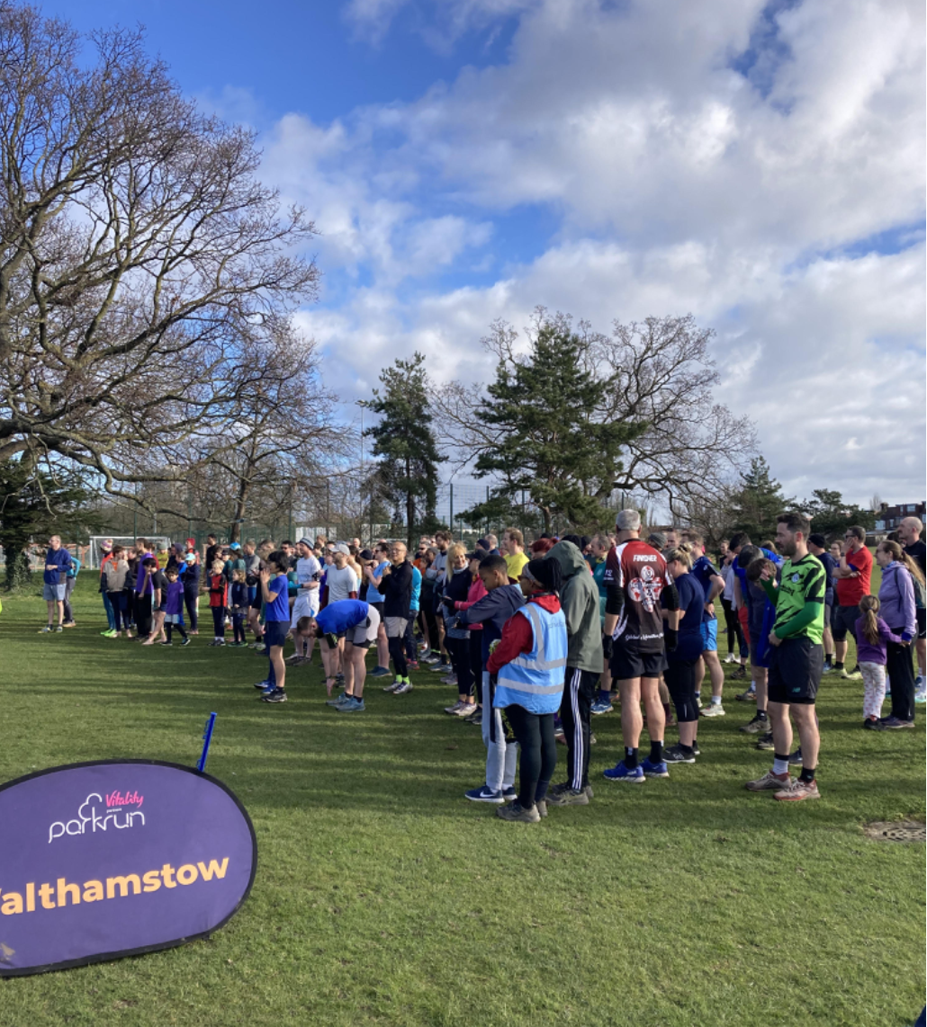 Runners and volunteers gathered at the start of Walthamstow parkrun beside a parkrun banner
